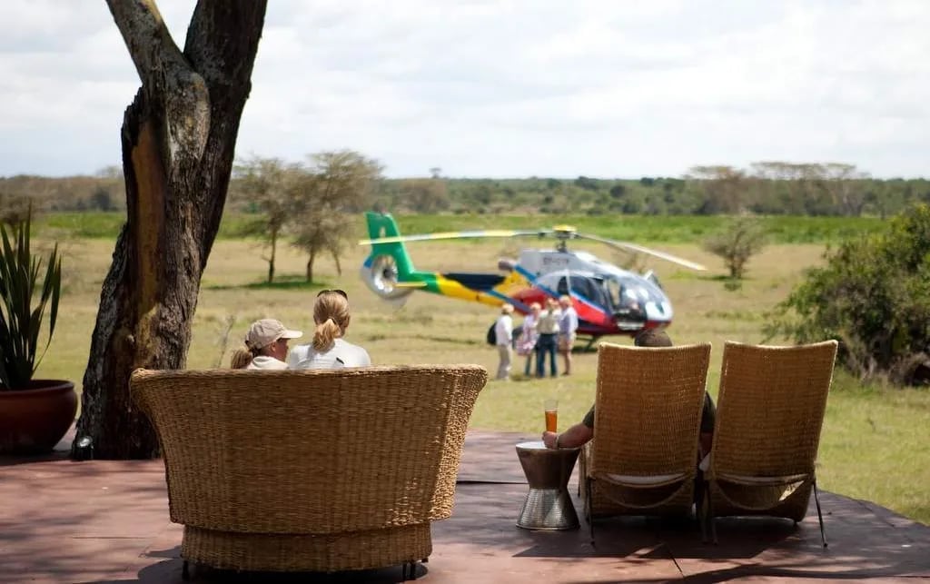 Guests at safari lodge watch helicopter landing on airstrip across the savanna landscape